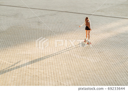 Young woman rides a skateboard under the sunset. 69233644