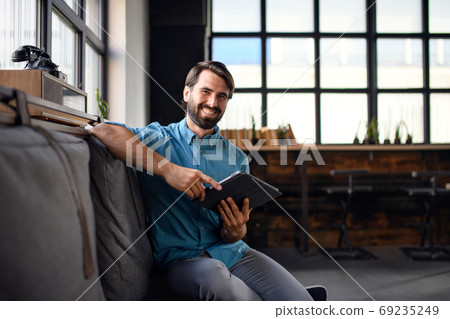 Portrait of young businessman with tablet indoors in office, looking at camera. 69235249