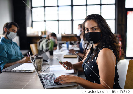 Portrait of young businesspeople with face masks working indoors in office. 69235250