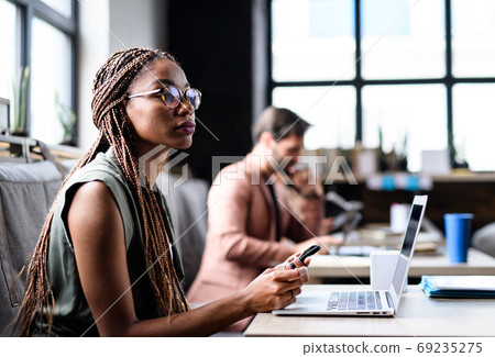 Portrait of young businesspeople with laptop working indoors in office. 69235275