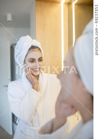 Young woman with facial mask looking in the mirror and looking happy Young woman with facial mask looking in the mirror and looking happy 69237853