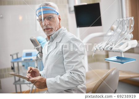 Competent dental specialist taking notes at work 69238919