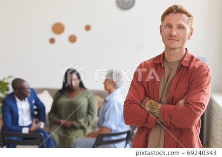 Tattooed Man Posing against Group Discussion Tattooed Man Posing against Group Discussion 69240343