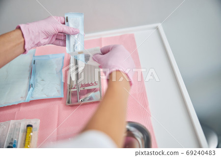 Woman doctor removing sterile surgical tools from the package Woman doctor removing sterile surgical tools from the package 69240483
