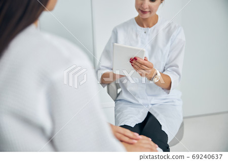 Dermatologist with a gadget sitting by her client 69240637
