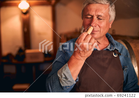Handsome winemaker enjoying the scent of wine cork 69241122