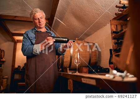 Handsome man with bottle of wine standing in wine cellar 69241127