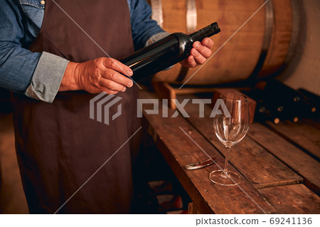 Male winemaker in apron holding bottle of wine Male winemaker in apron holding bottle of wine 69241136