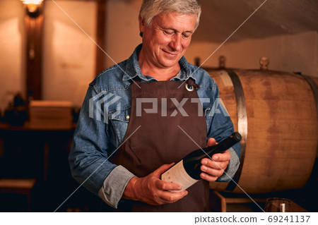 Handsome man in apron holding bottle of wine Handsome man in apron holding bottle of wine 69241137