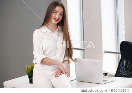 Happy businesswoman leaning on desk in office, office europe Happy businesswoman leaning on desk in office, office europe 69241534