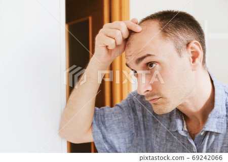 Young man looking at mirror worry about balding. 69242066