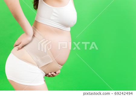 Close up of supporting bandage against backache on pregnant woman in underwear at green background with copy space Mother is suffering from pain in the back. Orthopedic abdominal support belt concept Close up of supporting bandage against backache on pregnant woman in underwear at green background with copy space Mother is suffering from pain in the back. Orthopedic abdominal support belt concept 69242494