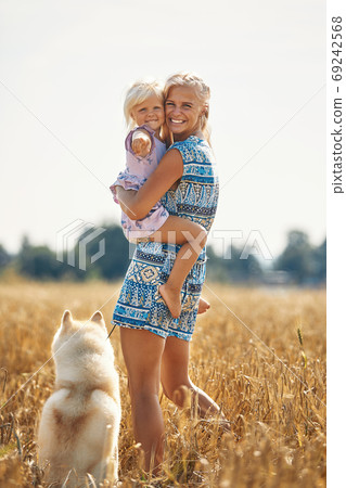 Cute baby girl with mom and dog on wheat field. Happy young family enjoy time together at the nature. Mom, little baby girl and dog husky resting outdoors. togetherness, love, happiness concept. Cute baby girl with mom and dog on wheat field. Happy young family enjoy time together at the nature. Mom, little baby girl and dog husky resting outdoors. togetherness, love, happiness concept. 69242568