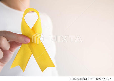 Young female holding yellow gold ribbon awareness symbol for endometriosis, suicide prevention, sarcoma bone cancer, bladder cancer, liver cancer and childhood cancer concept. Health care. Copy space. 69243997
