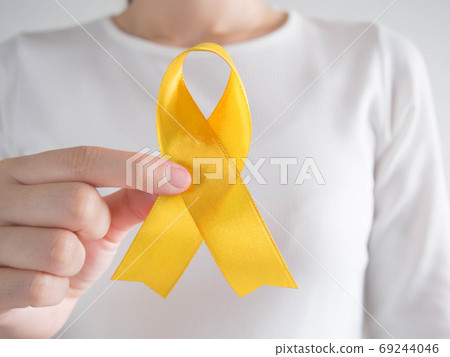 Young female holding yellow gold ribbon awareness symbol for endometriosis, suicide prevention, sarcoma bone cancer, bladder cancer, liver cancer and childhood cancer concept. Young female holding yellow gold ribbon awareness symbol for endometriosis, suicide prevention, sarcoma bone cancer, bladder cancer, liver cancer and childhood cancer concept. 69244046