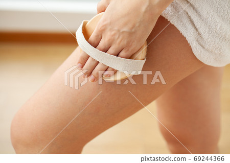 Cellulite treatment, woman arm holding dry brush to top of her leg. 69244366