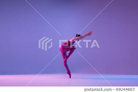 Young and graceful ballet dancer isolated on purple studio background in neon light Young and graceful ballet dancer isolated on purple studio background in neon light 69244667