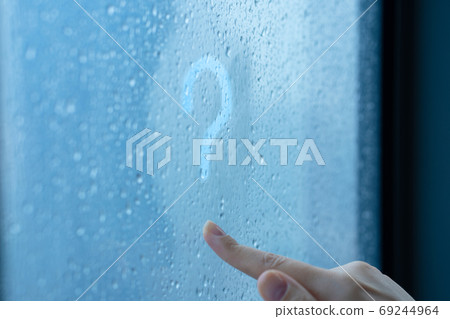Female hand draws a question mark on a foggy window during the rain. A glass in drops of water. 69244964