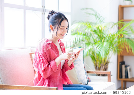 A woman who operates a smartphone while relaxing on the sofa. A woman who operates a smartphone while relaxing on the sofa. 69245163