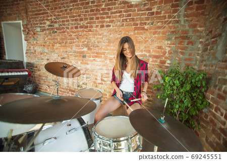 Woman recording music, singing and playing drums while sitting in loft workplace or at home Woman recording music, singing and playing drums while sitting in loft workplace or at home 69245551