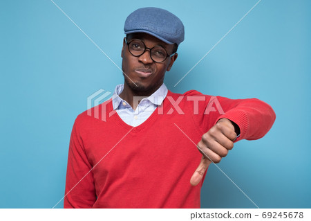 African man giving thumbs down gesture, looking with negative facial expression 69245678