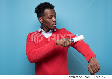 African man holding a white sticky brush for cleaning clothes from dust 69245752