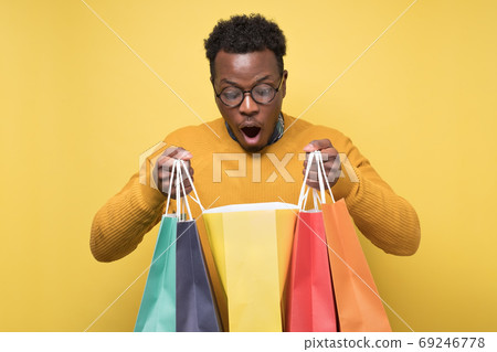 Shocked african young man holding shopping bags being surprises. Shocked african young man holding shopping bags being surprises. 69246778