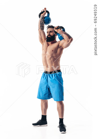 Muscular shirtless tattooed bearded male athlete bodybuilder workout with kettlebell on a white background. 69249319
