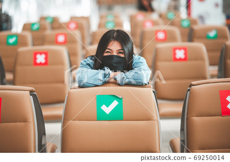 Happy woman wearing mask sitting on social distancing chair 69250014