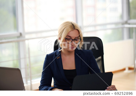 smiling blonde businesswoman with glasses using laptop in the office smiling blonde businesswoman with glasses using laptop in the office 69252896