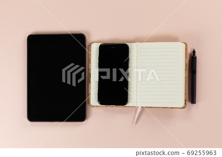 View of a tablet and phone with notebook and pen on pink background 69255963