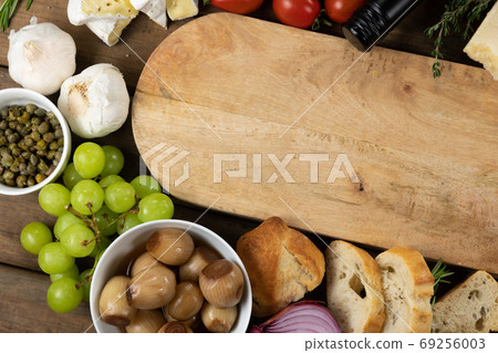 View of a wooden cutting board with bread, cheese, sausage, fruits and wine on a wooden surface 69256003