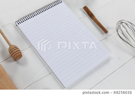 View of a composition with a notebook with wooden spoon and whisker on white wooden surface 69256038