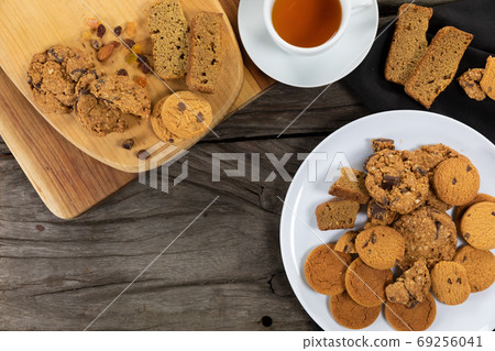 View of some cookies put on a white plate and a wooden cutting board, arranged on on a textured wood 69256041