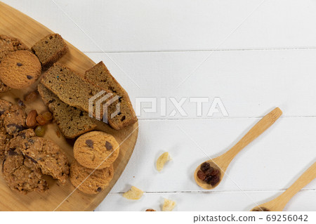 View of cookies put on a wooden cutting board on wooden surface and spoons with dried fruits 69256042