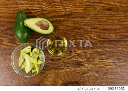 View of two avocados, olive oil bottle and cut avocado in a bowl on wood table background View of two avocados, olive oil bottle and cut avocado in a bowl on wood table background 69256062