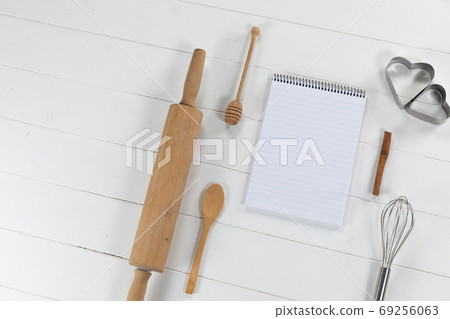 View of a composition of a notebook with cookie cutters, whisker and rolling pin on white surface View of a composition of a notebook with cookie cutters, whisker and rolling pin on white surface 69256063