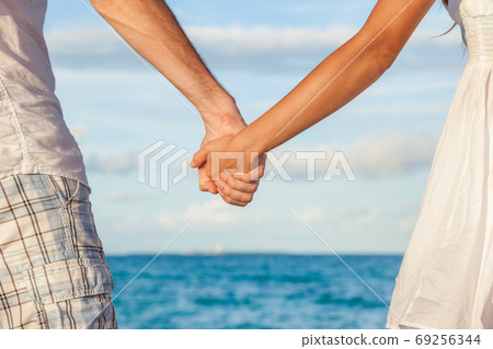 Romantic couple holding hands on beach sunset during travel. Happy woman and man in romance on honeymoon romance in beautiful sun light. 69256344
