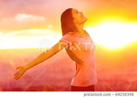 Happy people - carefree woman enjoying free nature at sunset. Freedom, serenity, wellness and spirituality concept - Asian girl with open arms in ecstatic enjoyment praising life to the sky. 69256348