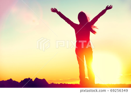 Happy celebrating winning success woman at sunset or sunrise standing elated with arms raised up above her head in celebration of having reached mountain top summit goal during hiking travel trek. Happy celebrating winning success woman at sunset or sunrise standing elated with arms raised up above her head in celebration of having reached mountain top summit goal during hiking travel trek. 69256349
