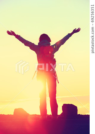 Happy hiker freedom having reached summit goal with success at sunset. Silhouette of woman with backpack celebrating winning standing at mountain top with arms up in celebration during hiking travel. Happy hiker freedom having reached summit goal with success at sunset. Silhouette of woman with backpack celebrating winning standing at mountain top with arms up in celebration during hiking travel. 69256351