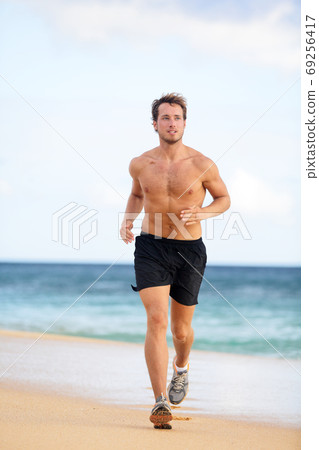 Beach fitness man runner running training cardio. Healthy lifestyle male athlete doing exercise living an active life working out on sunset beach with ocean background topless in shorts. 69256417