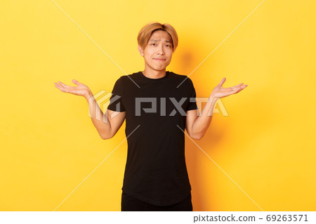 Portrait of confused and indecisive attractive korean guy, shrugging and pouting upset, standing yellow background Portrait of confused and indecisive attractive korean guy, shrugging and pouting upset, standing yellow background 69263571