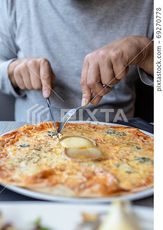 Man eating delicious cheesy pizza in the restaurant with fork and knife Man eating delicious cheesy pizza in the restaurant with fork and knife 69270778