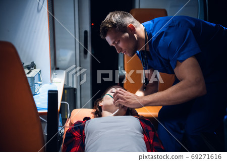 Young paramedic in a blue uniform gives an oxygen mask to a woman lying on a stretcher 69271616