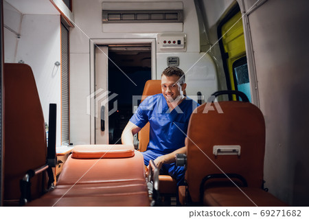 Positive paramedic sitting in the ambulance car and smiling at the camera with a toothy smile Positive paramedic sitting in the ambulance car and smiling at the camera with a toothy smile 69271682