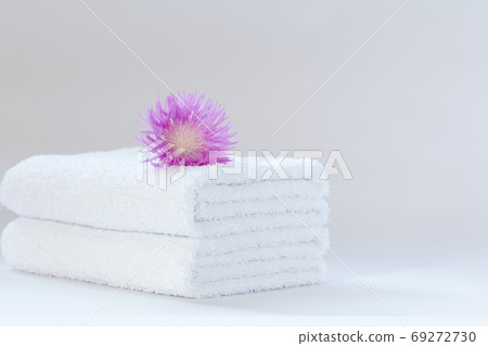 Two white neatly folded terry towels with a pink cornflower flower on a light background. 69272730