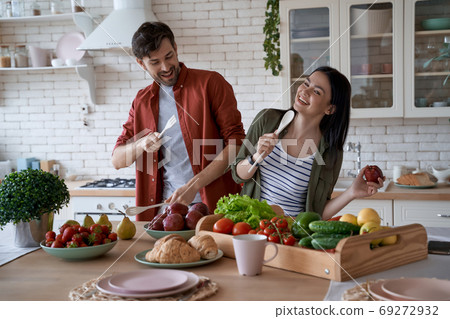 Enjoying cooking together. Young happy family couple, wife and husband having fun while preparing healthy food in the modern kitchen at home 69272932