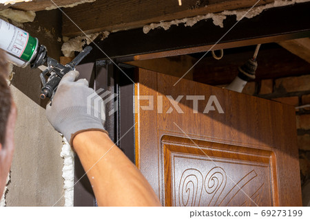 The worker foams and insulates the door, uses a carpenter's foam gun, a close-up of the work process. The worker foams and insulates the door, uses a carpenter's foam gun, a close-up of the work process. 69273199