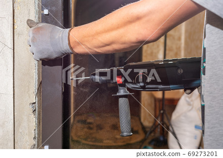 The carpenter drills holes in the wall and the metal door frame with a drill, later screws the screws and fastens the door frame to the wall. The carpenter drills holes in the wall and the metal door frame with a drill, later screws the screws and fastens the door frame to the wall. 69273201